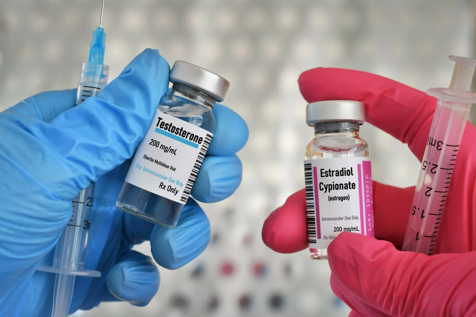 Gloved hands holding testosterone and estradiol vials with syringes