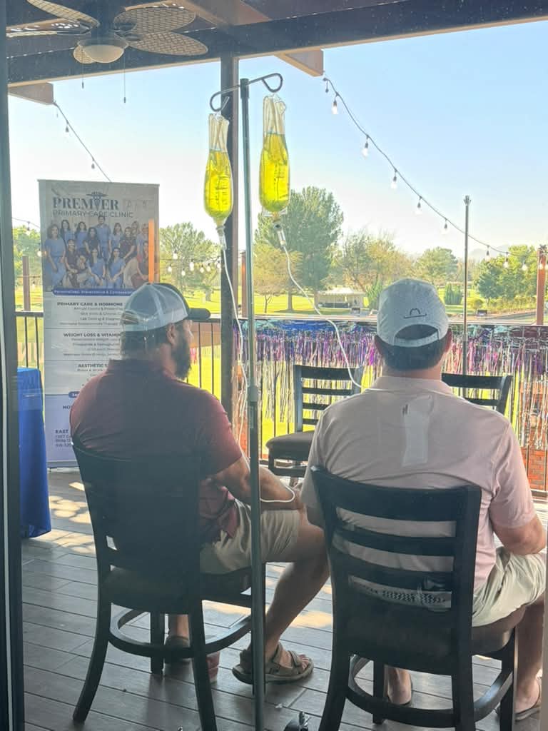 Two clients seated beside infusion equipment and a Premier banner on a terrace