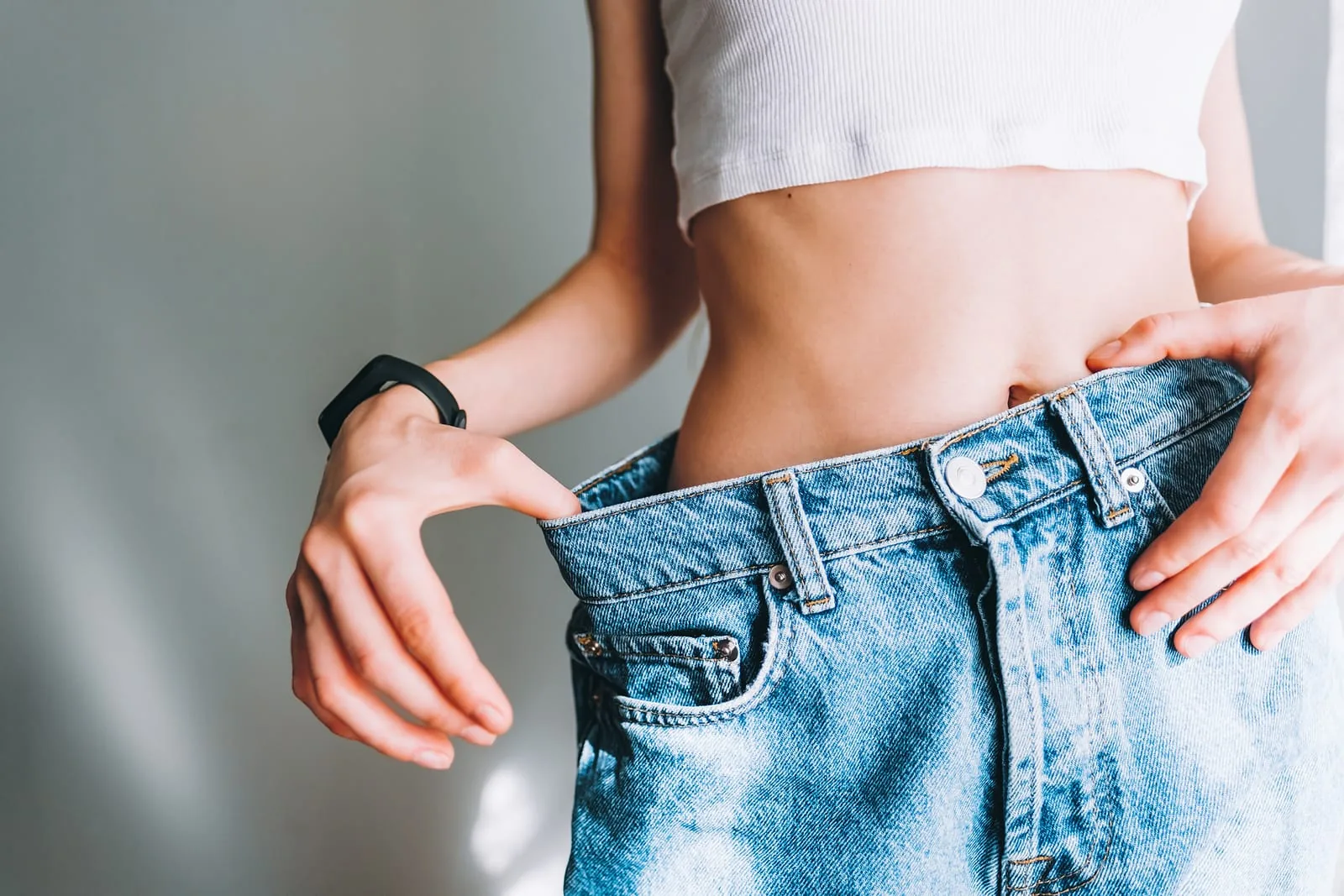 Woman holding out the waistband of jeans that are now too big